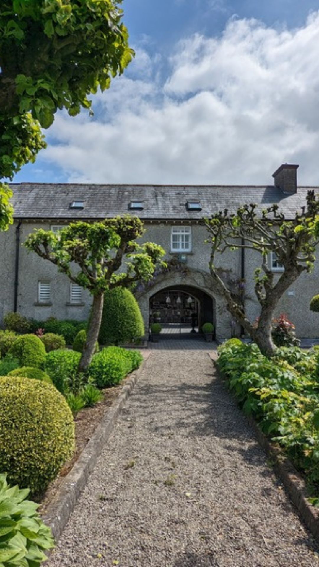 The arched entrance to Aluna Yoga Studio at Bishopsland House, framed by clipped trees and a gravel garden path