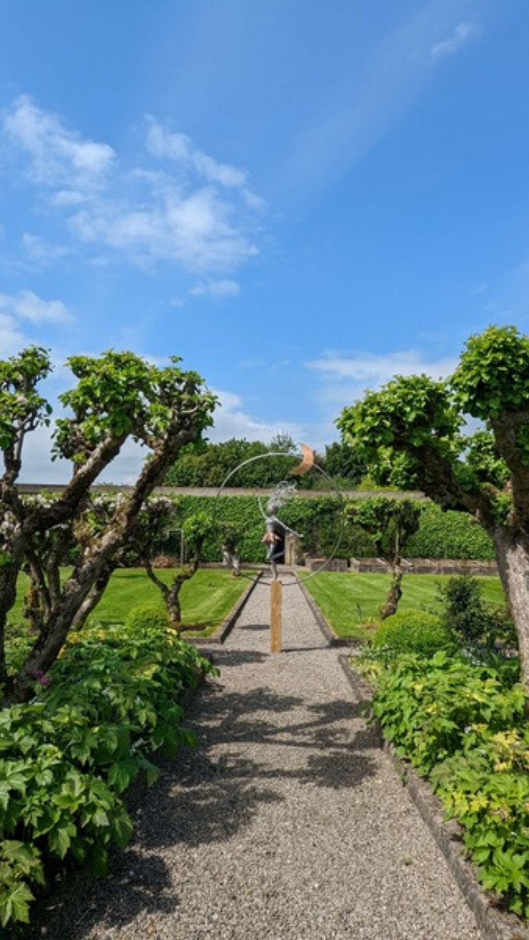 Gravel path through a walled garden towards a moon sculpture