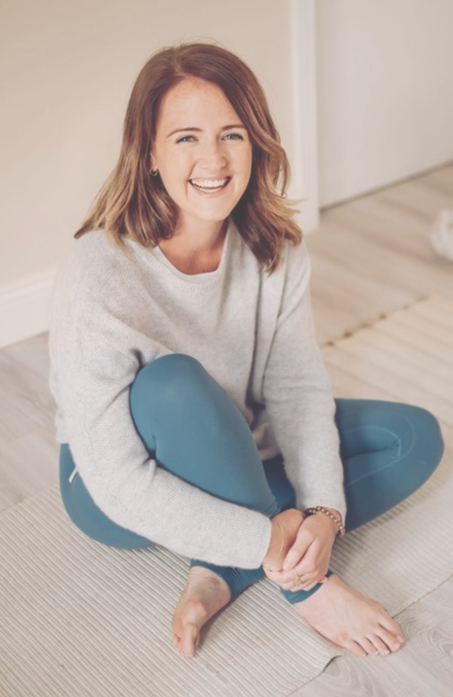 Andrea, owner of Aluna Yoga, sitting cross-legged on a yoga mat and smiling